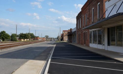 Cordele, Georgia streetscape with a freshly sealed asphalt lot beside low-rise brick commercial buildings and rail tracks.