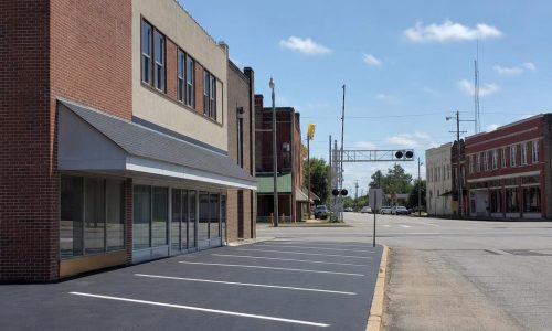 Waycross commercial street with brick storefronts beside a freshly coated asphalt parking area.